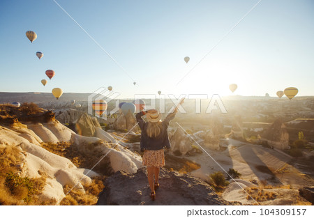 Young attractive girl stands on the mountain with flying air balloons. View from the back. Cappadocia. 104309157