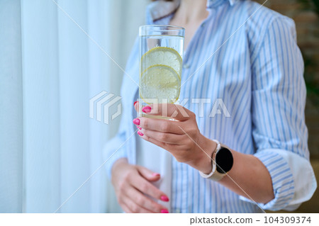 Close-up of glass of water with lemon in young woman's hand Close-up of glass of water with lemon in young woman's hand 104309374
