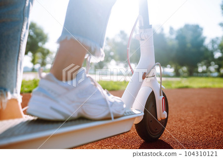 Legs of woman riding electric kick scooter. Ecological transportation concept. 104310121