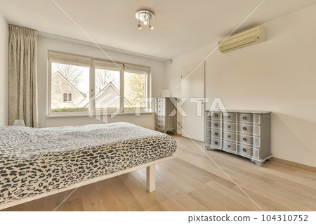 a bedroom with a bed, dresser and window in the back ground is light wood planks on the floor 104310752