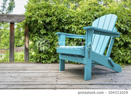 empty Adirondack chair on a wooden backyard deck, summer scenery with a green vine empty Adirondack chair on a wooden backyard deck, summer scenery with a green vine 104311029