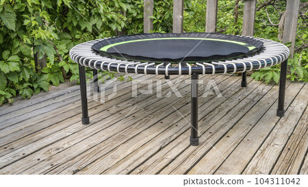 mini trampoline for fitness exercising and rebounding in a backyard patio, summer scenery 104311042