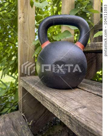 heavy iron competition kettlebell for weight training on wooden rustic stairs in backyard, home gym and fitness concept 104311083