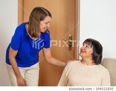 Young caregiver helping senior woman at home. Caring nurse assisting her middle aged female patient. 104312850