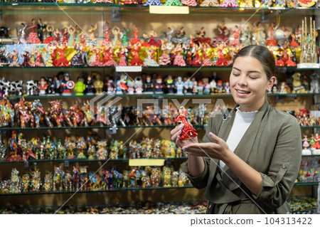 Young woman looks at figurine of Spanish dancer 104313422