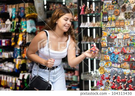 Female buyer holds in hands tests souvenir magnet in memorable gifts shop Female buyer holds in hands tests souvenir magnet in memorable gifts shop 104313430