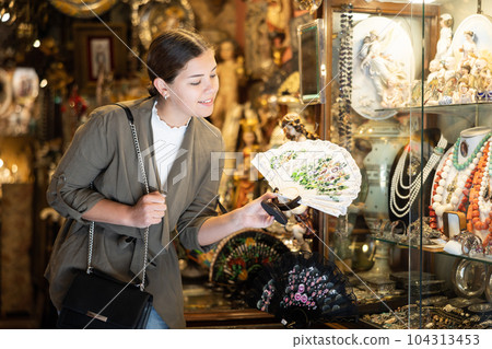Smiling female tourist inspecting oriental fans in antiques shop 104313453