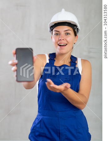 Young woman in work overalls posing with phone Young woman in work overalls posing with phone 104313580