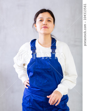 Positive young female construction worker in blue jumpsuit Positive young female construction worker in blue jumpsuit 104313581