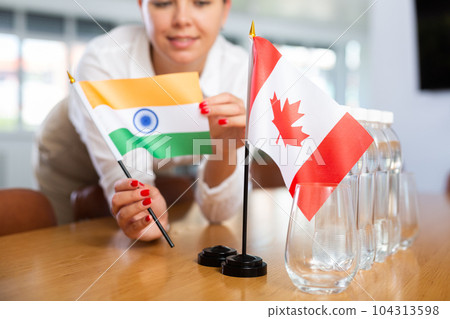 Little flag of Canada on table and flag of India put next to it by young woman Little flag of Canada on table and flag of India put next to it by young woman 104313598