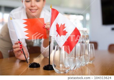 Little flag of Canada on table and flag of Bahrain put next to it by young woman Little flag of Canada on table and flag of Bahrain put next to it by young woman 104313624