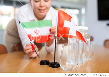 Little flag of Switzerland on table and flag of Iran put next to it by young woman 104313727