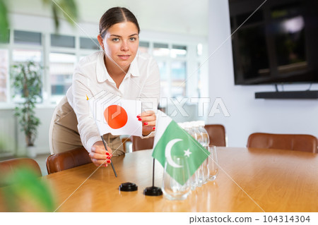 Young woman putting flags of Japan and Pakistan on table in office 104314304