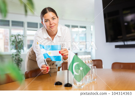 Positive young woman putting little flag of Argentina on table next to the flag of Pakistan Positive young woman putting little flag of Argentina on table next to the flag of Pakistan 104314363