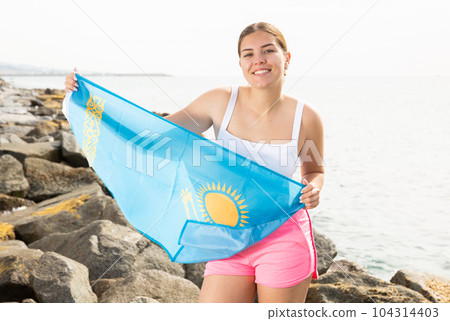 Young woman holding Kazakhstan waving flag at coastline against of sunny sea Young woman holding Kazakhstan waving flag at coastline against of sunny sea 104314403
