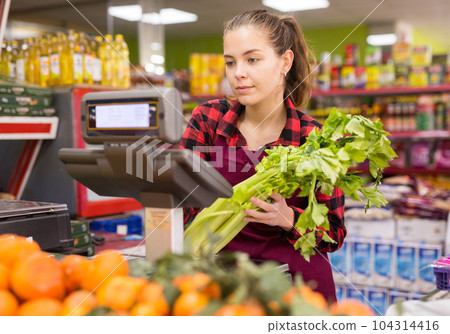 Young saleswoman weighs greens on a scale Young saleswoman weighs greens on a scale 104314416