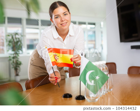 Positive young woman putting little flag of Spain on table next to the flag of Pakistan 104314432