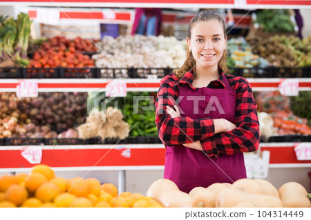 Friendly woman vegetable shop seller posing behind a counter Friendly woman vegetable shop seller posing behind a counter 104314449