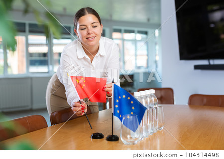 Young woman puts China and EU flags on table in office 104314498