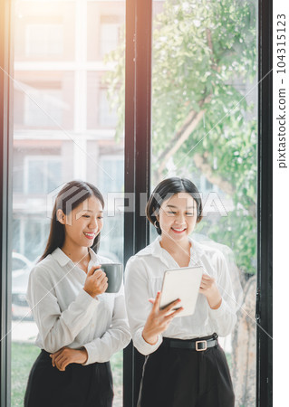 Two office workers talking with experienced colleague while using digital tablet in office, Colleagues discuss business. Two office workers talking with experienced colleague while using digital tablet in office, Colleagues discuss business. 104315123
