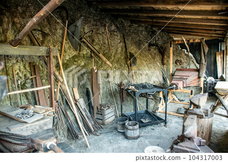 View of traditional blacksmith's shop for forging medieval iron, with furnace and an ancient bellows blower View of traditional blacksmith's shop for forging medieval iron, with furnace and an ancient bellows blower 104317003