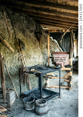 View of traditional blacksmith's shop for forging medieval iron, with furnace and an ancient bellows blower 104317005