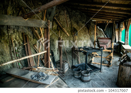 View of traditional blacksmith's shop for forging medieval iron, with furnace and an ancient bellows blower 104317007