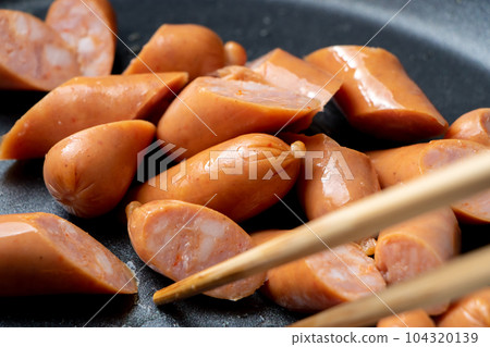A cooking scene where diagonally cut wiener sausages are fried in a frying pan. A cooking scene where diagonally cut wiener sausages are fried in a frying pan. 104320139