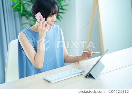 Woman making a phone call while looking at a computer screen Woman making a phone call while looking at a computer screen 104321812