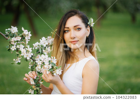 Portrait of a young beautiful woman in the spring flowers of an apple tree 104322083