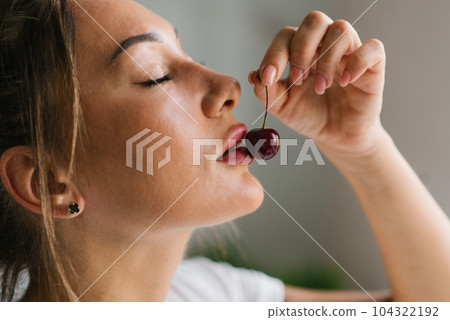 Attractive young woman eats fresh cherry, healthy berry close-up 104322192