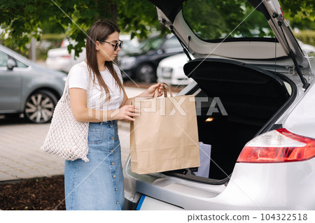 Portrait of attractive young woman stand by open trunk with shopping bag Portrait of attractive young woman stand by open trunk with shopping bag 104322518