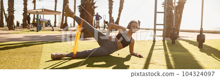 Active female stretching exercising equipment at athletic field 104324097