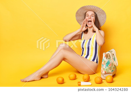 Positive woman wearing one piece swimming suit posing isolated over yellow background keeps hands near mouth screaming with happy expression making announcement. 104324280