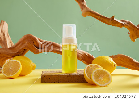 Mockup scene for advertising cosmetic of lemon extract with yellow bottle with fresh lemon slices and dry twigs on green background. Lemons are a good source of vitamin C and antioxidants Mockup scene for advertising cosmetic of lemon extract with yellow bottle with fresh lemon slices and dry twigs on green background. Lemons are a good source of vitamin C and antioxidants 104324578