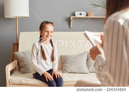 Smiling charming girl in psychologist office talking with doctor, schoolgirl patient psychotherapy consultation children trauma treatment professional help. 104324804
