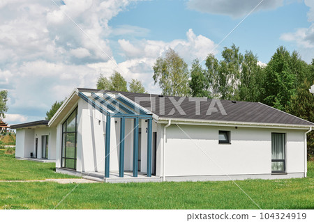 Side view of modern designed residential house, green lawn near building near the forest with beautiful blue sky on background. 104324919