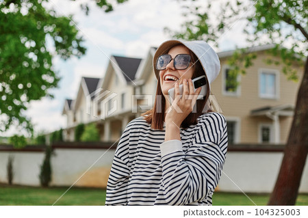 Urban stylish portrait of amazing joyful young woman in striped shirt panama and modern sunglasses walking in street in town. Cheerful emotions, enjoying sightseeing. Urban stylish portrait of amazing joyful young woman in striped shirt panama and modern sunglasses walking in street in town. Cheerful emotions, enjoying sightseeing. 104325003