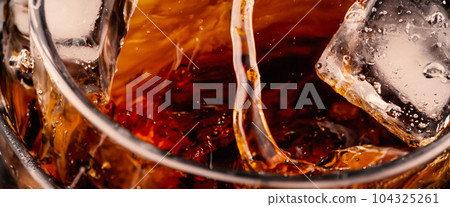 Splashing of Cola and Ice. Cola soda and ice splashing fizzing or floating up to top of surface. Close up of ice in cola water. Texture of carbonate drink with bubbles in glass. Cold drink background Splashing of Cola and Ice. Cola soda and ice splashing fizzing or floating up to top of surface. Close up of ice in cola water. Texture of carbonate drink with bubbles in glass. Cold drink background 104325261