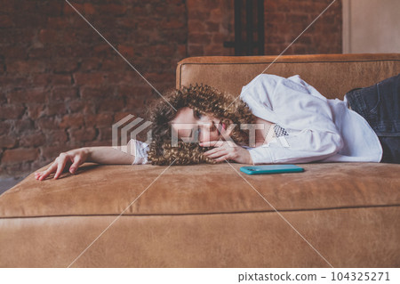 Beautiful glamorous woman in white shirt with curly hair resting on the sofa Beautiful glamorous woman in white shirt with curly hair resting on the sofa 104325271