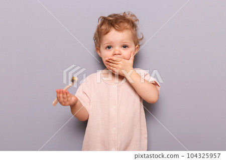 Surprised little girl holding toothbrush isolated on gray background learning daily dental hygiene holding toothbrush, kid's health and wellness, copy space for promotion. 104325957
