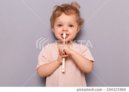 Adorable infant little girl holding toothbrush isolated on gray background brushing her teeth with tiny toothbrush looking at camera children oral care. 104325960