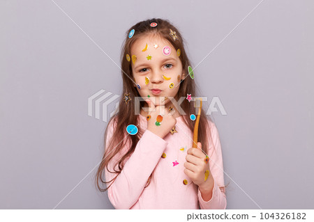 Cute pensive girl with her toothbrush standing isolated over gray background with toothbrush in hands, holding chin, thinking, having thoughtful expression. Cute pensive girl with her toothbrush standing isolated over gray background with toothbrush in hands, holding chin, thinking, having thoughtful expression. 104326182