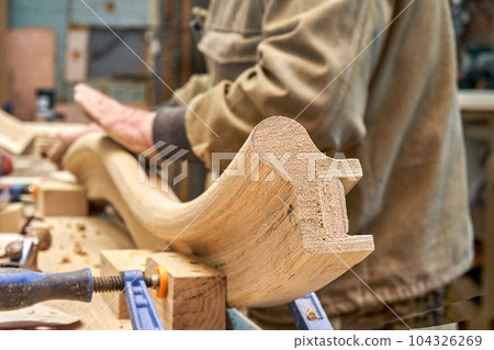 Carpenter sands bending wooden railing with sandpaper in workshop closeup. Senior master makes detail of spiral staircase for home interior 104326269