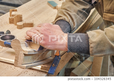 Carpenter sands bending wooden railing with sandpaper in workshop closeup. Senior master makes detail of spiral staircase for home interior 104326345