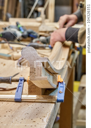 Carpenter sands bending wooden railing with sandpaper in workshop closeup. Senior master makes detail of spiral staircase for home interior Carpenter sands bending wooden railing with sandpaper in workshop closeup. Senior master makes detail of spiral staircase for home interior 104326351