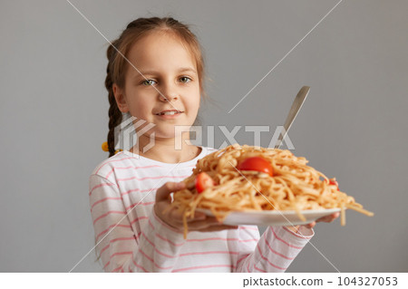 Cute smiling little kid girl with pigtails eating spaghetti holding big plate with pasta looking at camera waiting for dinner being extremely hungry. Cute smiling little kid girl with pigtails eating spaghetti holding big plate with pasta looking at camera waiting for dinner being extremely hungry. 104327053