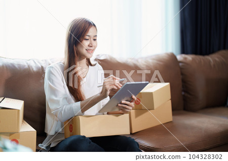 Starting small business entrepreneur of independent young Asian woman online seller is using tablet computer and taking orders to pack products for delivery to customers. SME delivery concept. 104328302