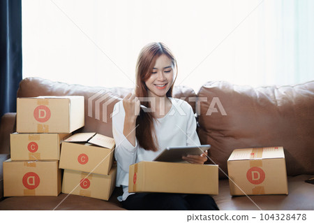 Starting small business entrepreneur of independent young Asian woman online seller is using tablet computer and taking orders to pack products for delivery to customers. SME delivery concept. 104328478