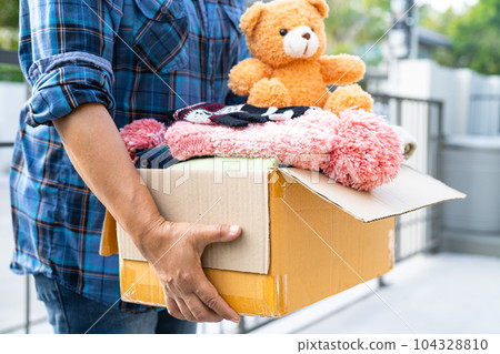 Volunteer woman provide clothing donation box with used clothes and doll to support help for refugee, homeless or poor people in the world. 104328810